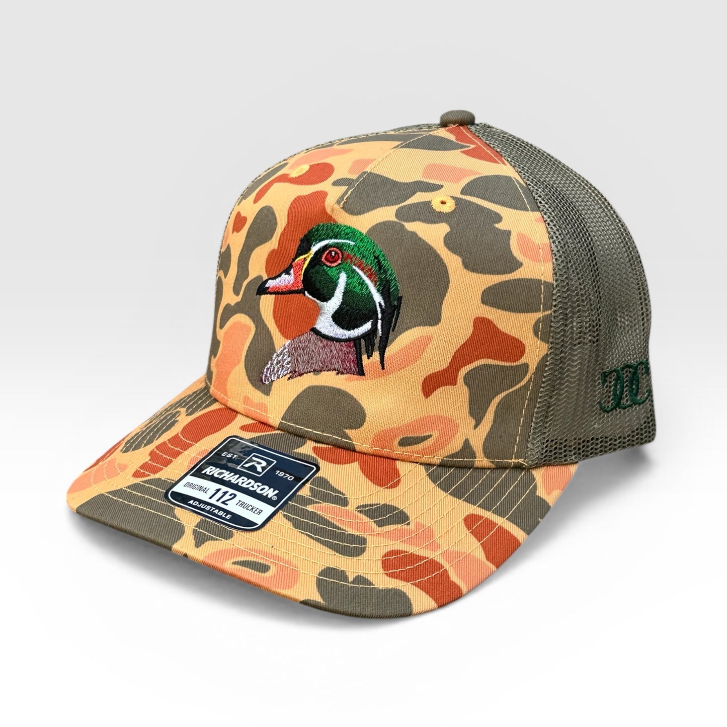 Orange and grey camouflage patterned cap with an embroidered wood duck design on a light gray background