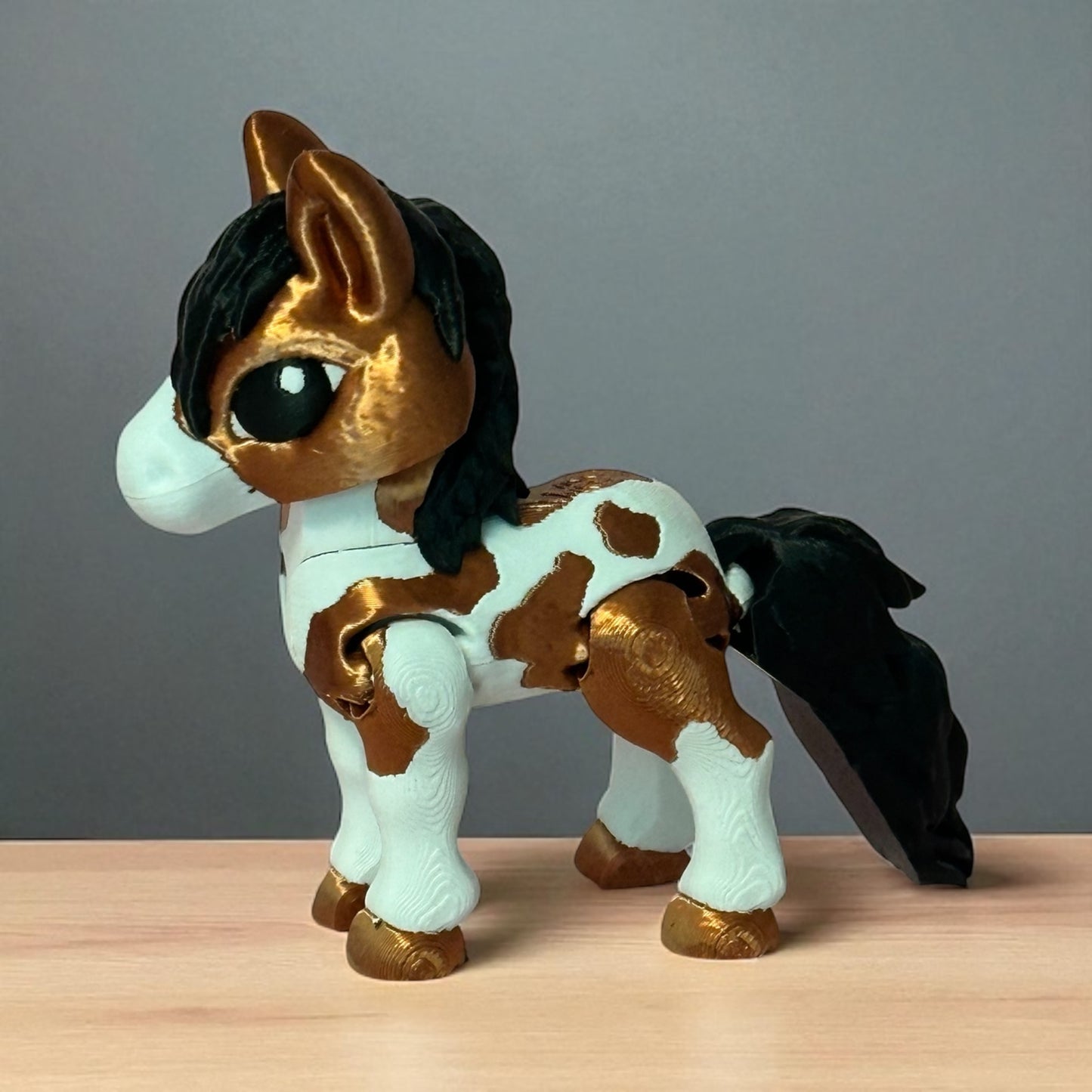 3d printed toy horse figurine with white and brown pattern on a wooden surface and gray background