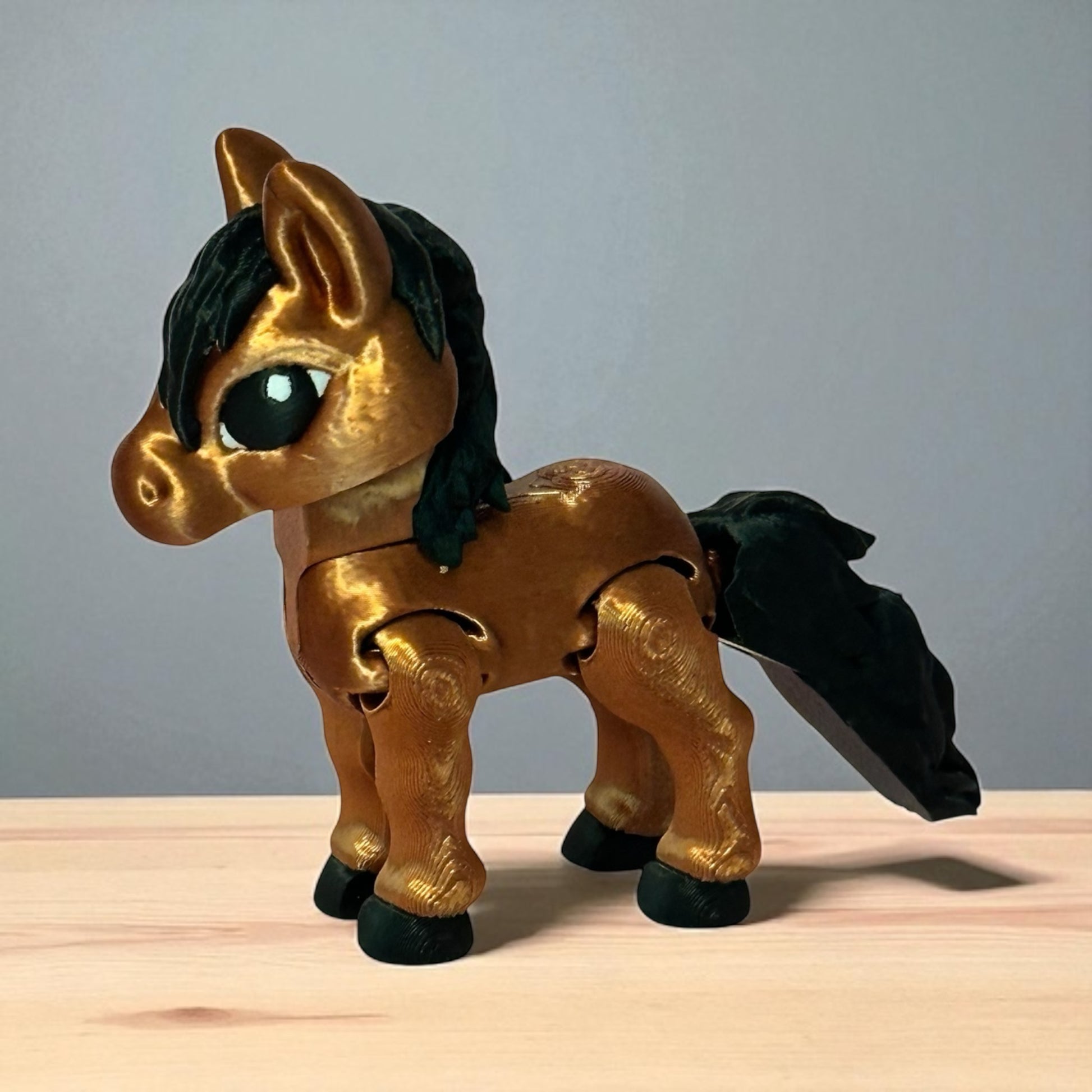 3d printed toy horse with golden brown body and black mane and tail on a wooden surface and gray background