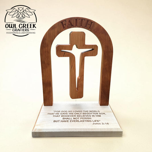A wooden Christian altar plaque featuring an arched cherry wood cross with the word 'FAITH' engraved at the top, mounted on a rectangular maple wood base with a Bible verse printed on it. The product is photographed against a plain beige background, with the Owl Creek Crafters logo in the upper left corner.