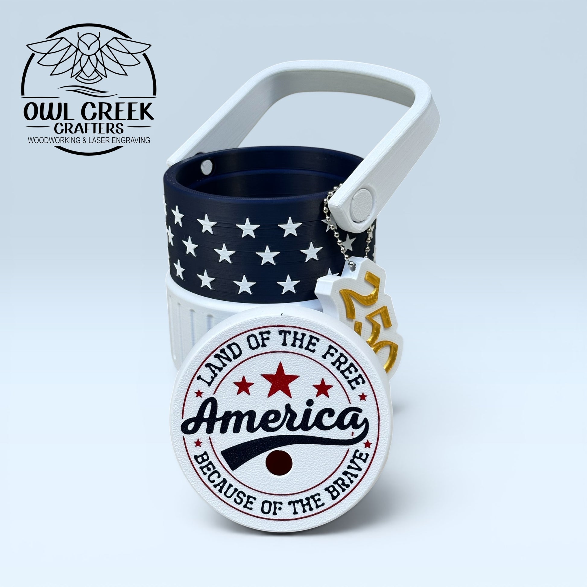 American flag-themed can cooler coozie and a '250' keychain, with a red white and blue lid that says 'America land of the free because of the brave', on a light gray background with the Owl Creek Crafters logo