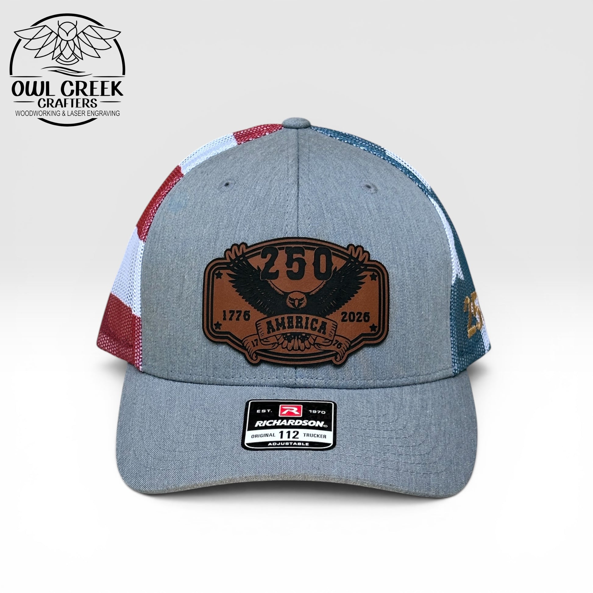Gray cap with a brown leather patch and red, white, and blue accents on a light gray background with the Owl Creek Crafters Logo