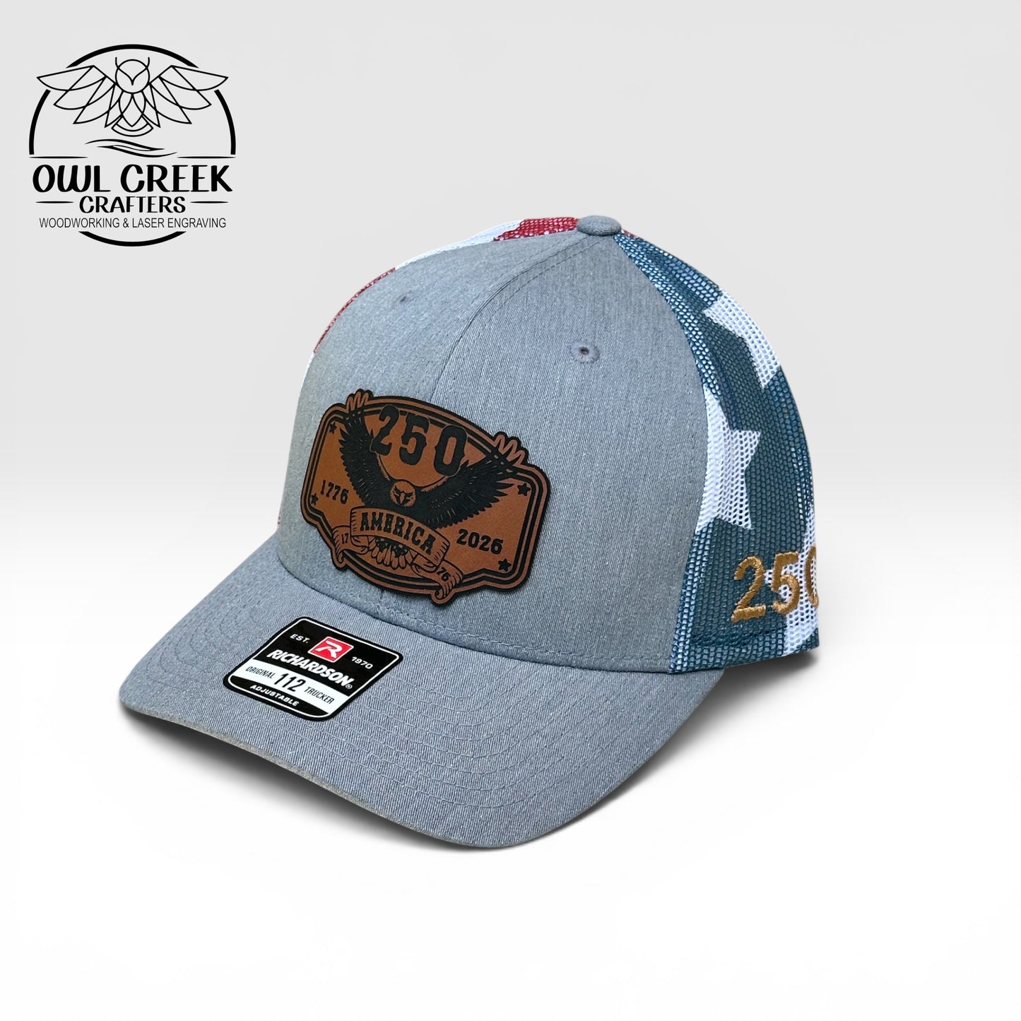 Gray cap with a brown leather patch and red, white, and blue accents on a light gray background with the Owl Creek Crafters Logo