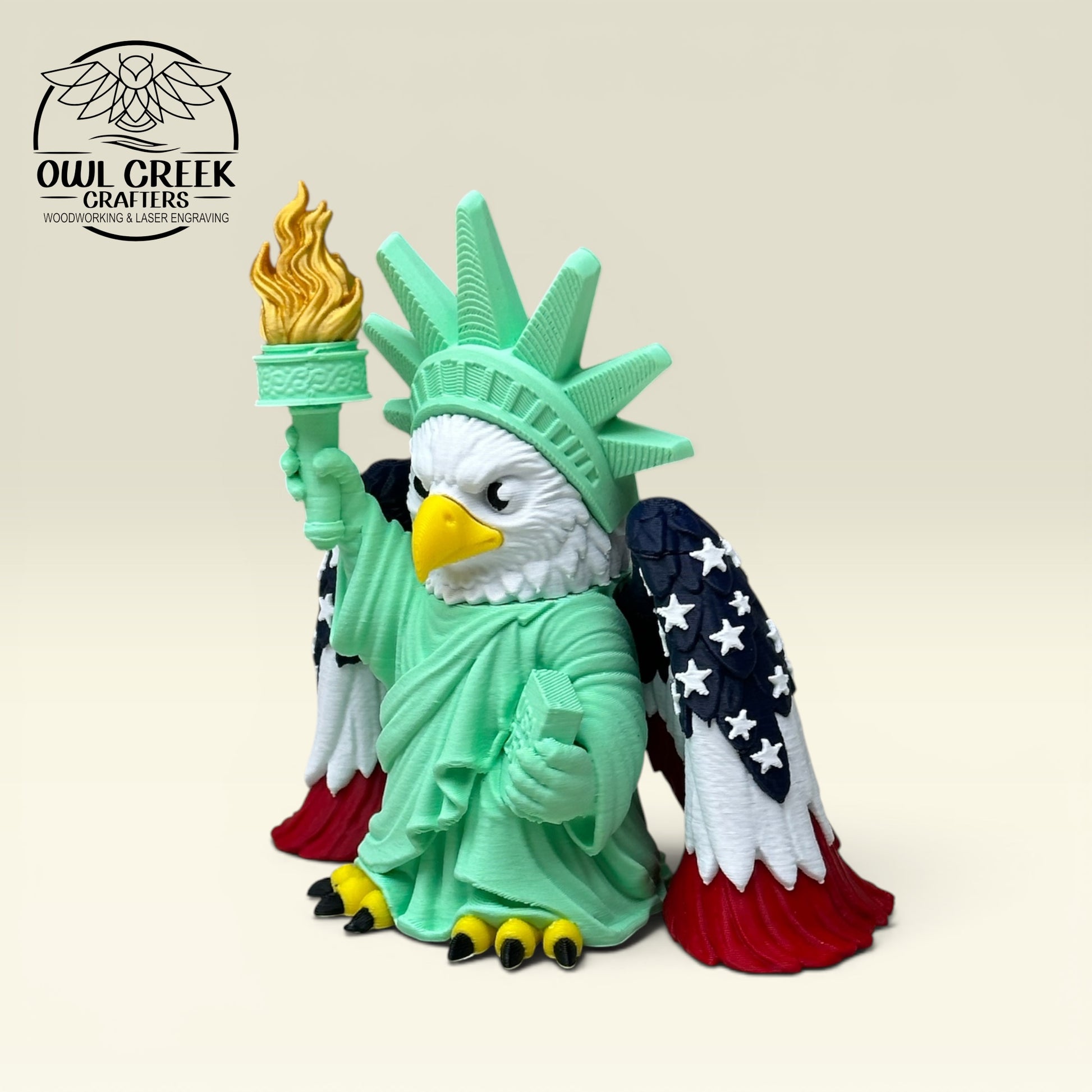 Bald eagle dressed as the Statue of Liberty with American flag wings, with a beige background and the Owl Creek Crafters Logo