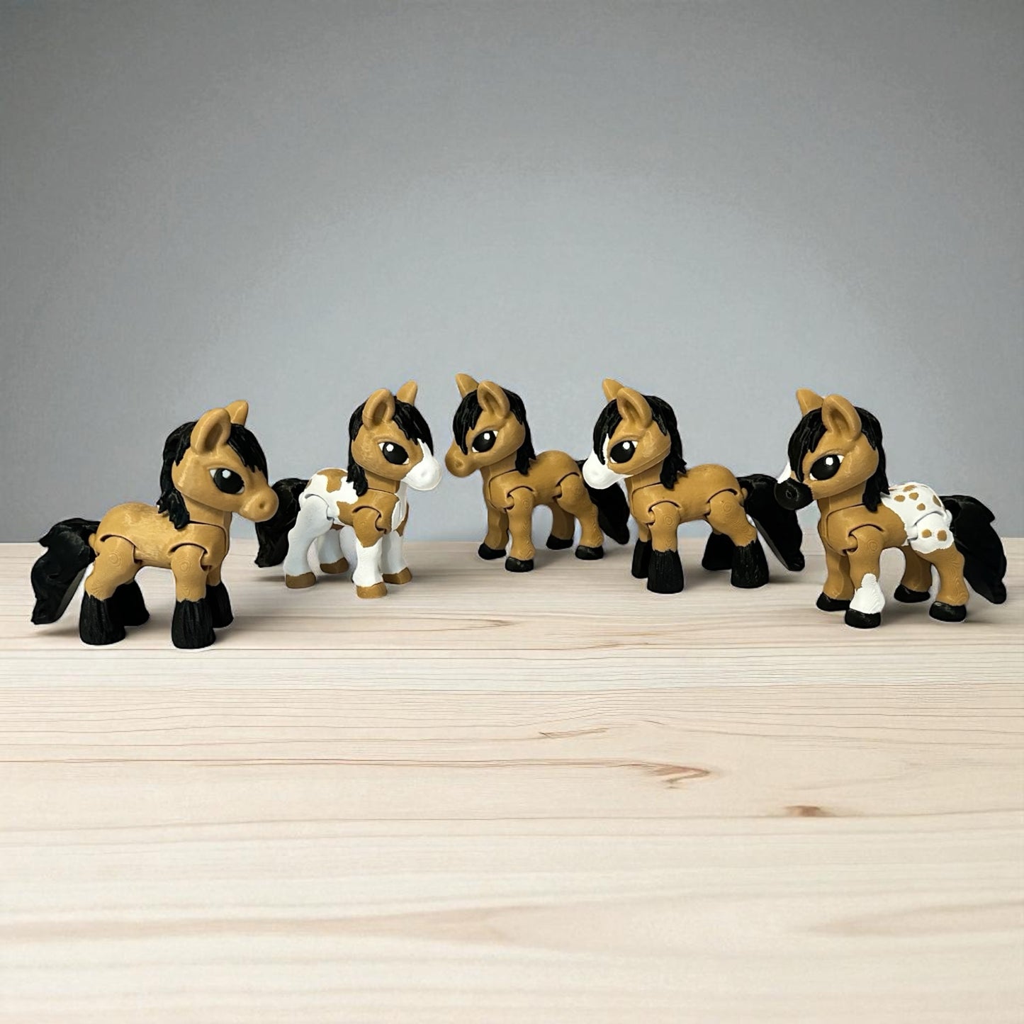 Set of five toy 3-d printed brown, black, and white horses on a wooden surface with a gray background