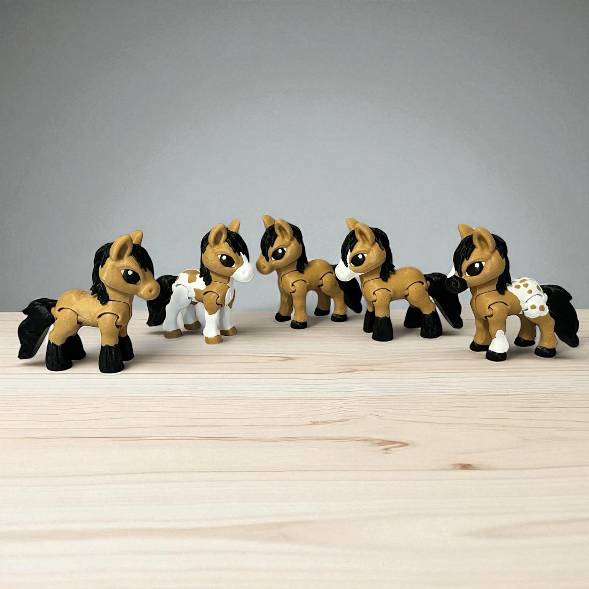 Set of five toy 3-d printed brown, black, and white horses on a wooden surface with a gray background