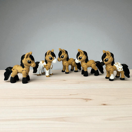 Set of five toy 3-d printed brown, black, and white horses on a wooden surface with a gray background