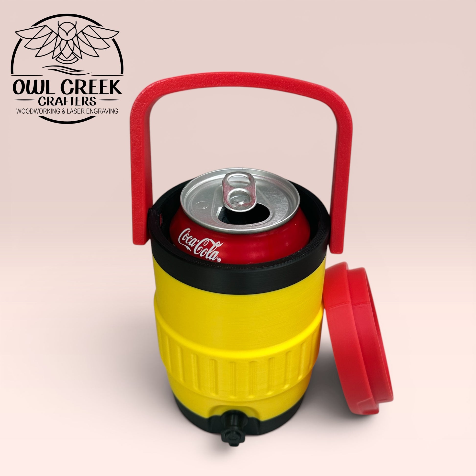 Yellow and black can cooler coozie with a red handle and lid sitting against the side, with a Coca-Cola can inside the coozie, on a beige background with the Owl Creek Crafters Logo