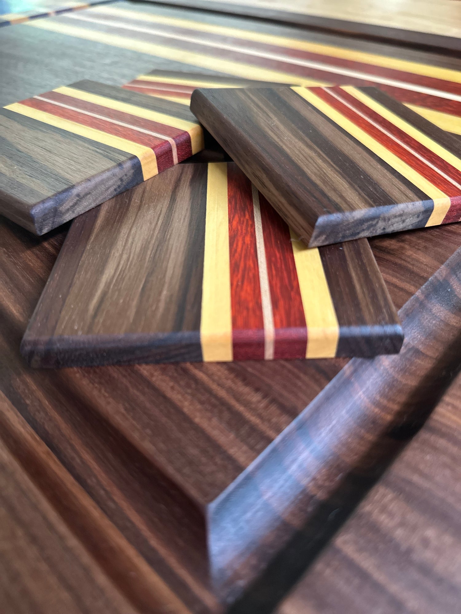 Set of wood coasters sitting on a matching cutting board. The coaster and cutting board have red, yellow, and brown woods.