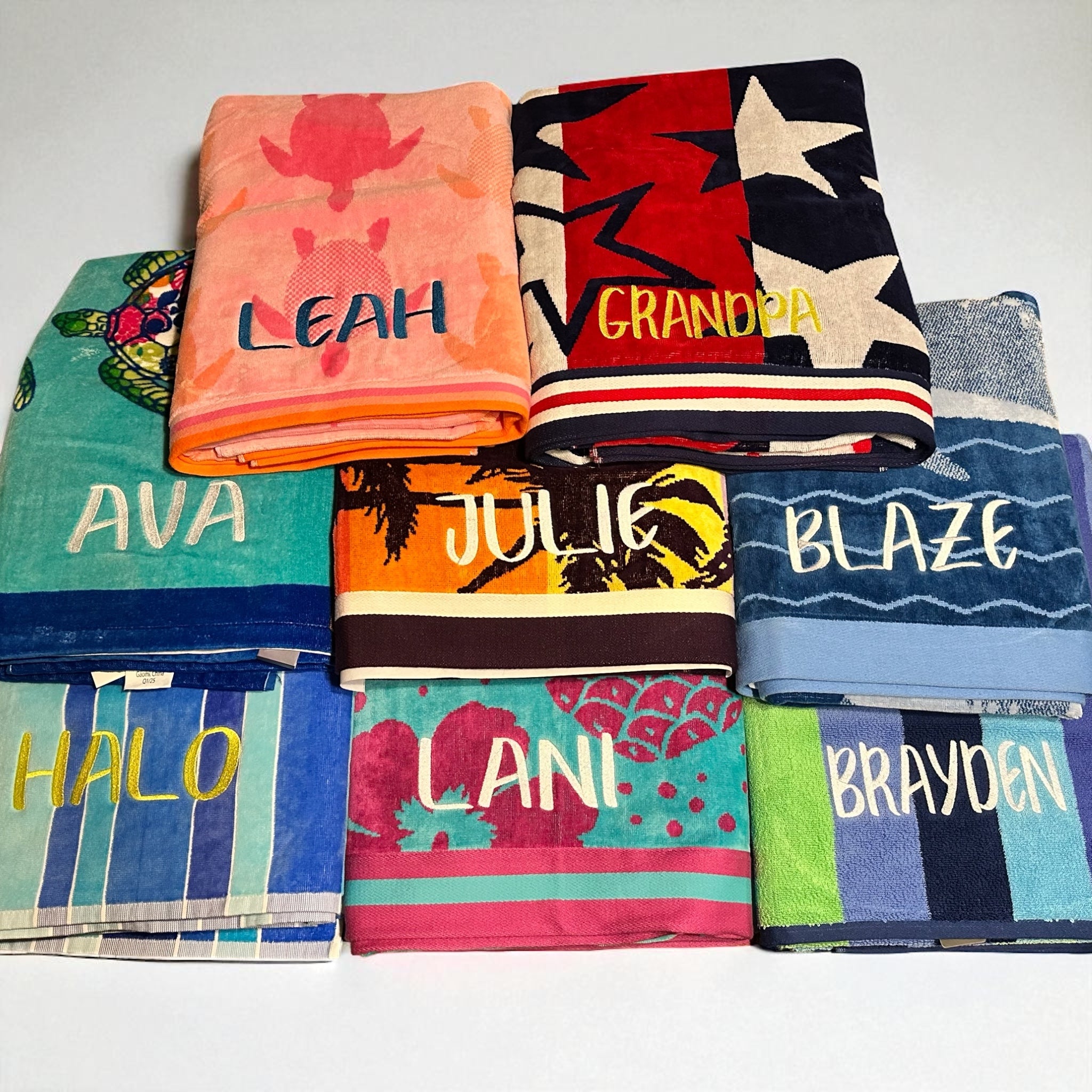 Stack of personalized beach towels with names embroidered on them, on a white background