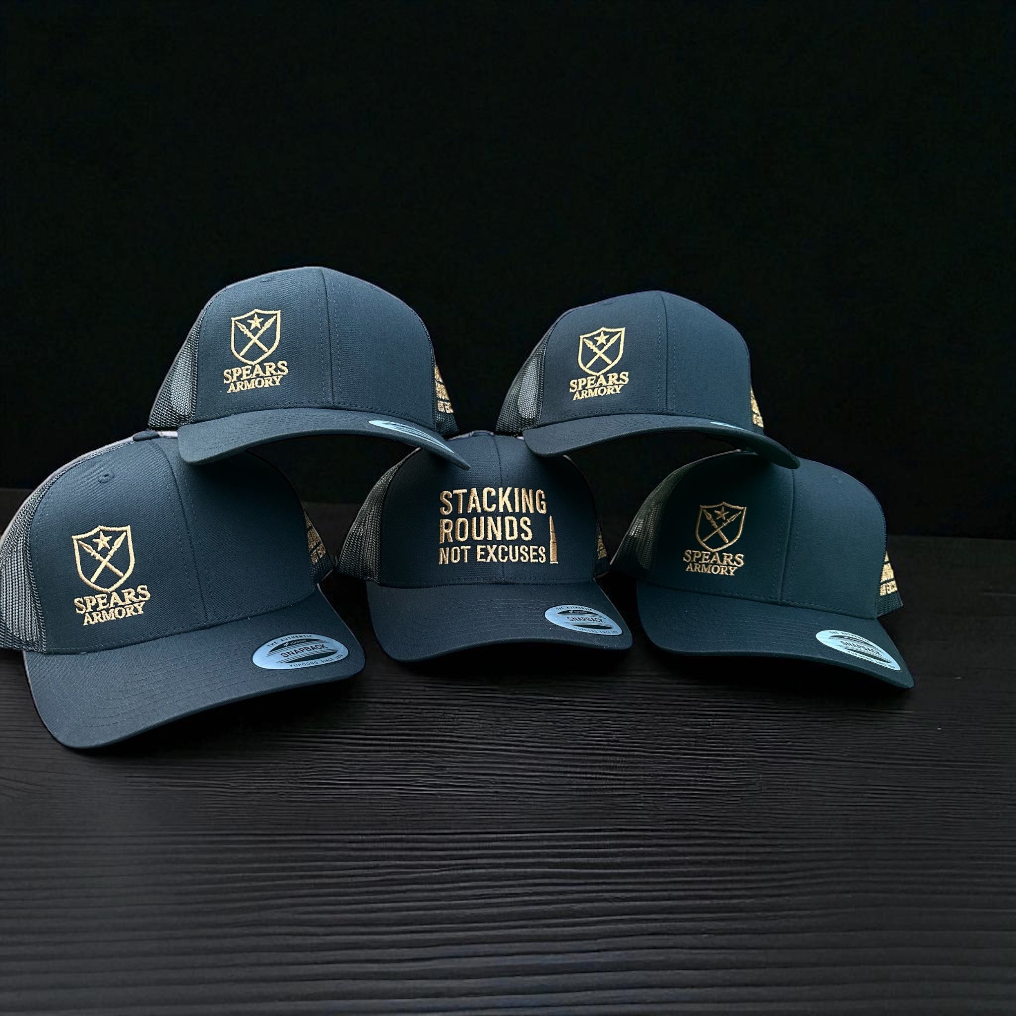 Four navy blue caps with gold embroidered text and branding on a black background