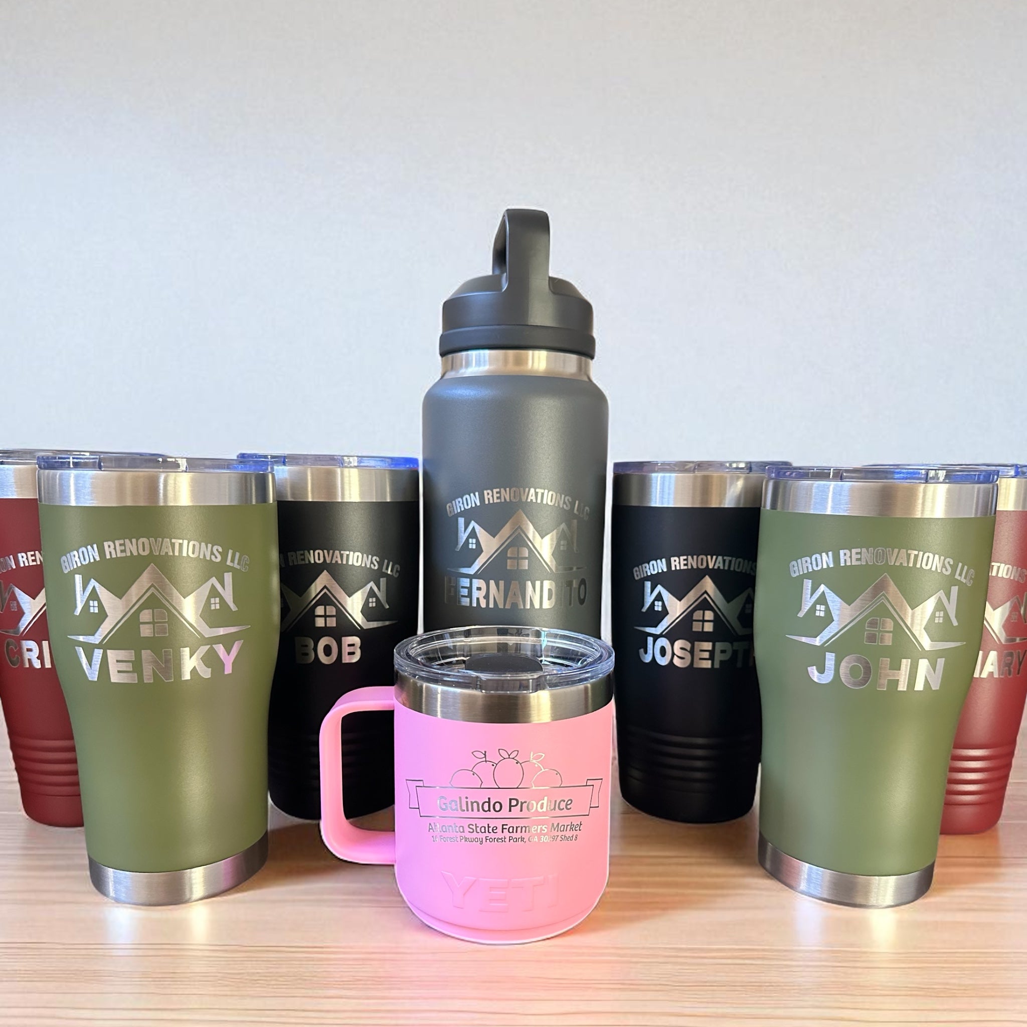 Collection of personalized tumblers and water bottles with engraved text on a wooden surface and grey background