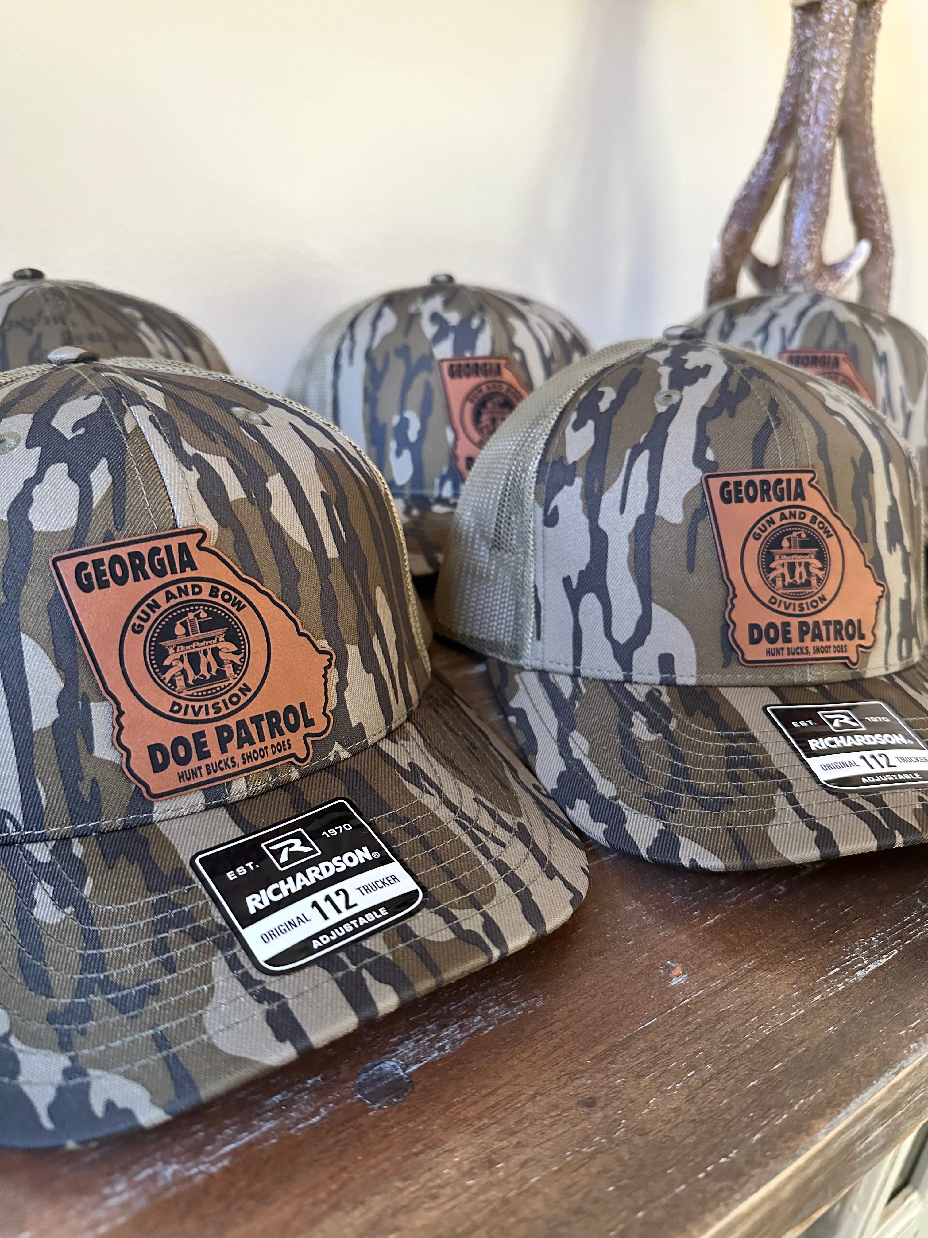 Camouflage hats with Georgia Doe Patrol logo leatherette patches on a wooden surface and beige background