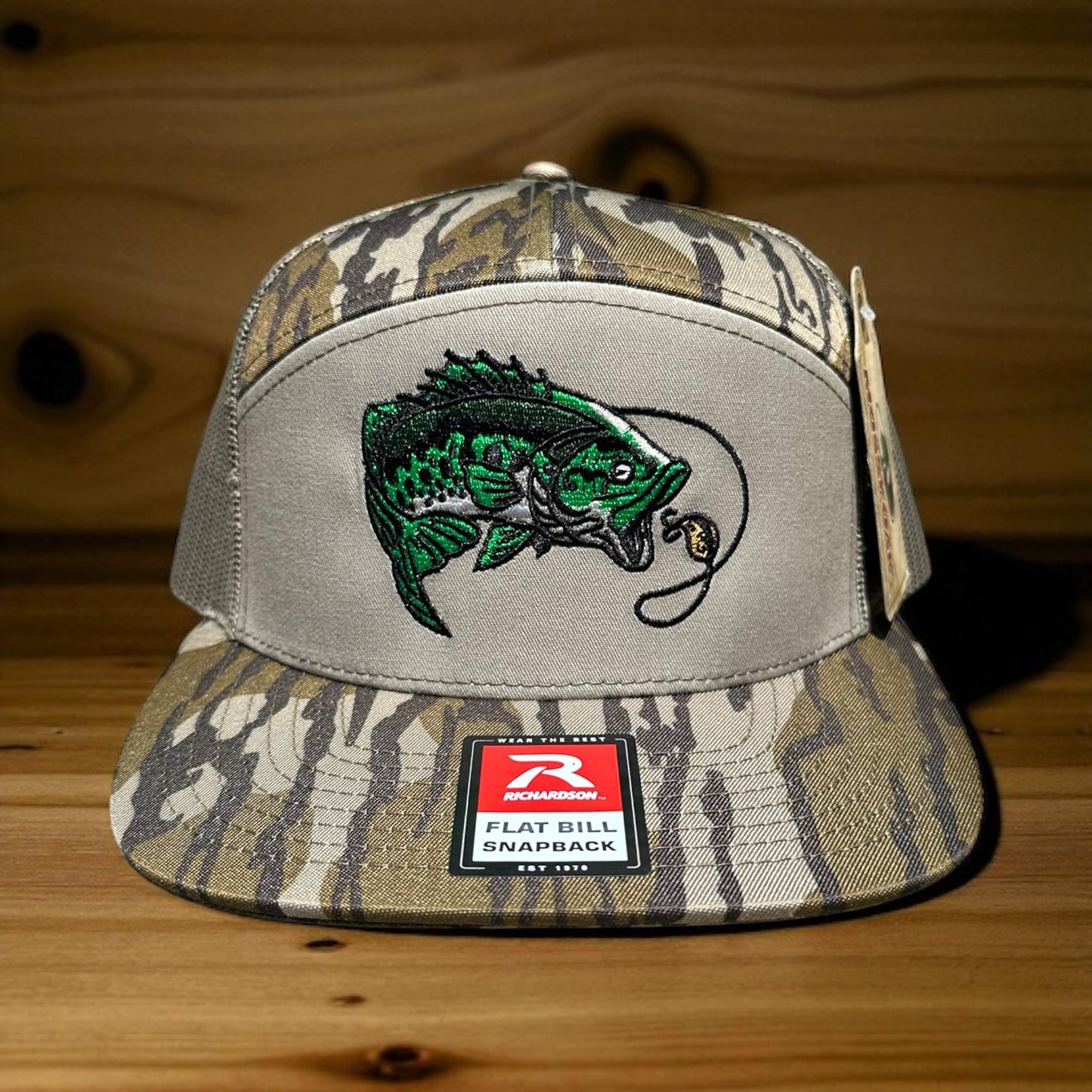 Camouflage cap with an embroidered fish design and a visible brand logo label on a wooden surface