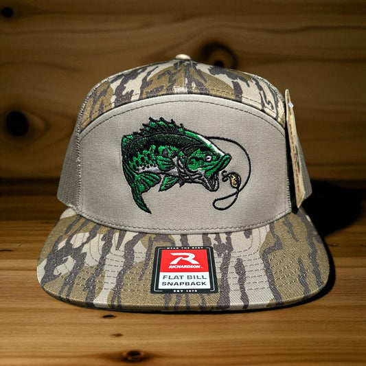 Camouflage cap with an embroidered fish design and a visible brand logo label on a wooden surface