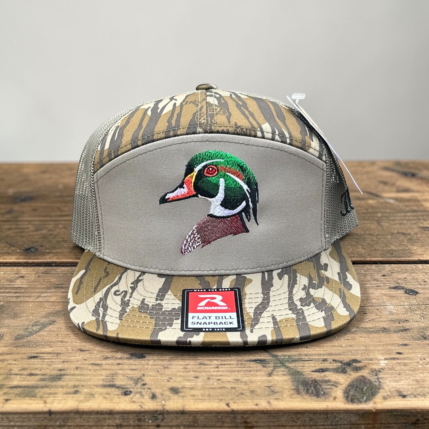 Bottomland camouflage pattern trucker cap with an embroidered wood duck embroidered logo on a wooden surface