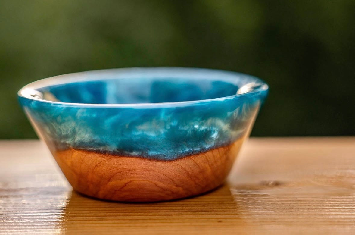 Handcrafted blue epoxy and wood trinket bowl sitting on a wood surface with a green background