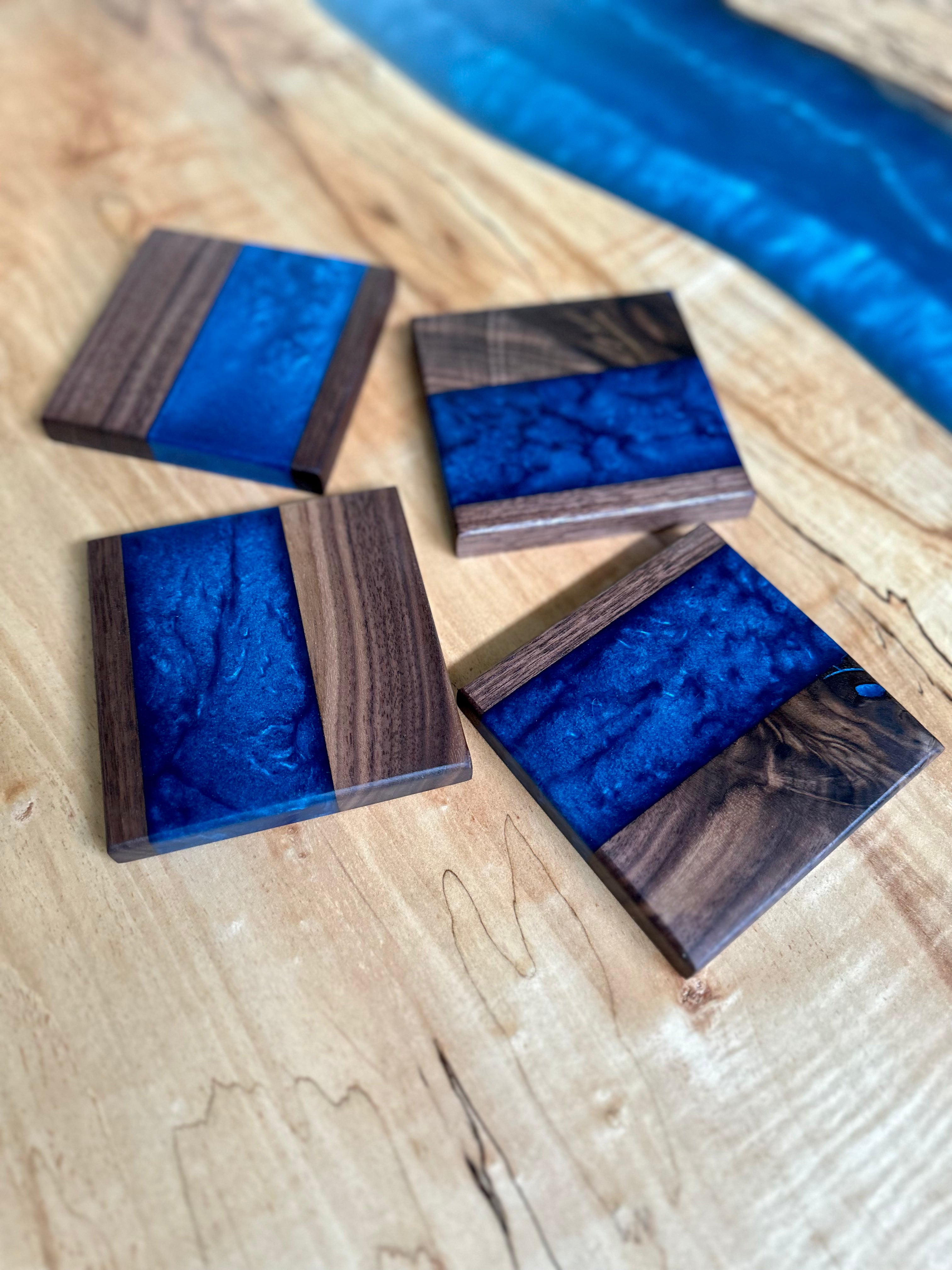 set of four handcrafted blue epoxy and wood coasters sitting on a wood and blue epoxy table