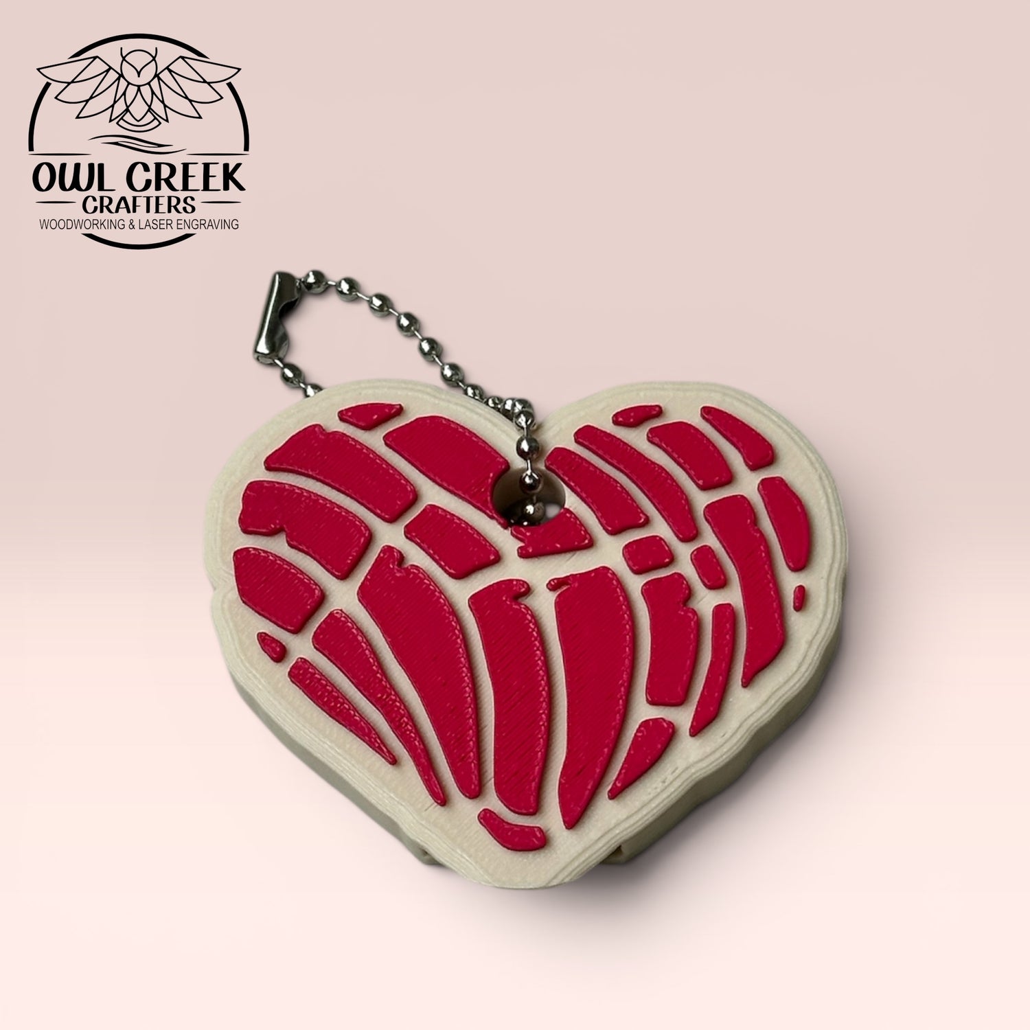 Heart-shaped keychain with magenta design on a beige background, and a 'Owl Creek Crafters' Logo