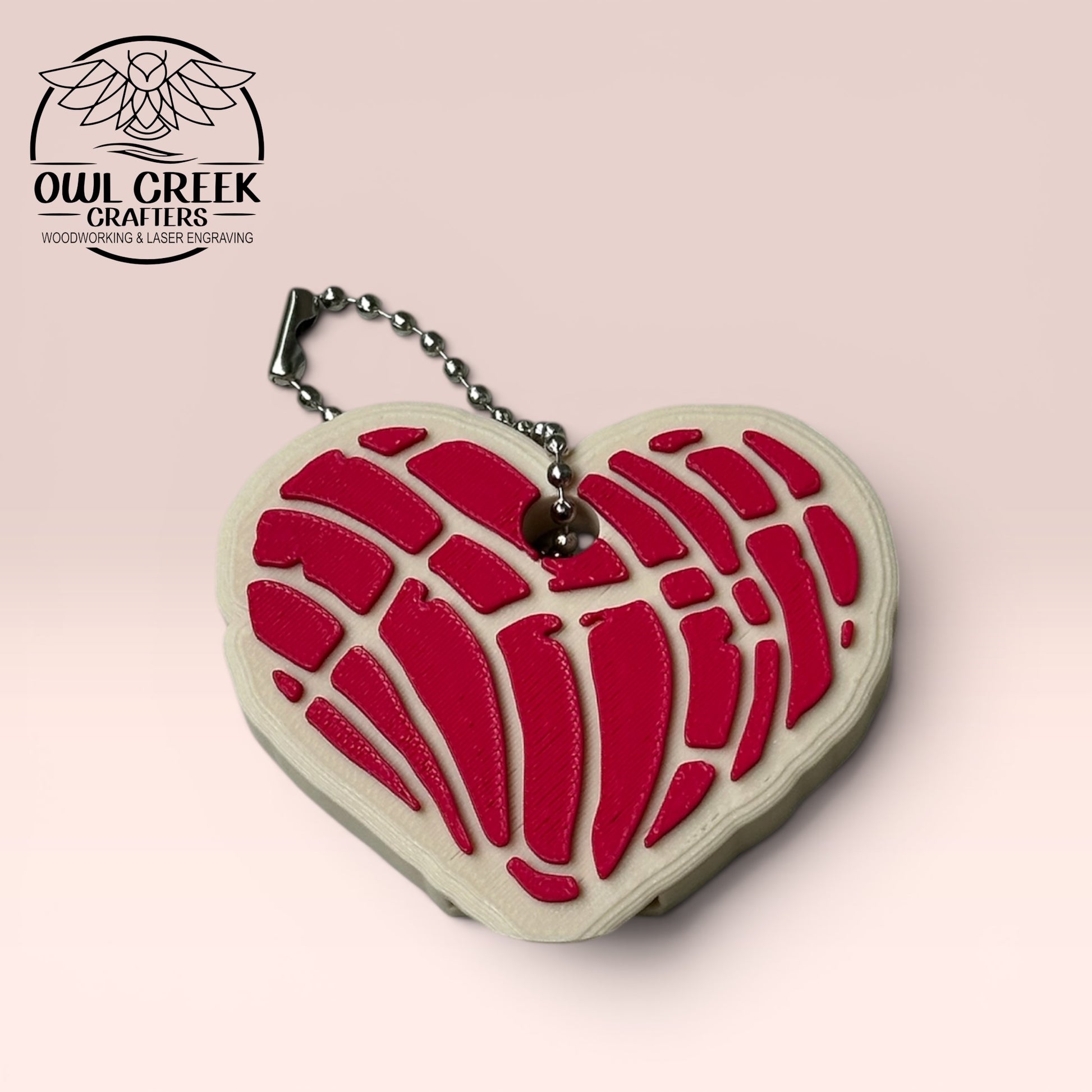 Heart-shaped keychain with magenta design on a beige background, and a 'Owl Creek Crafters' Logo