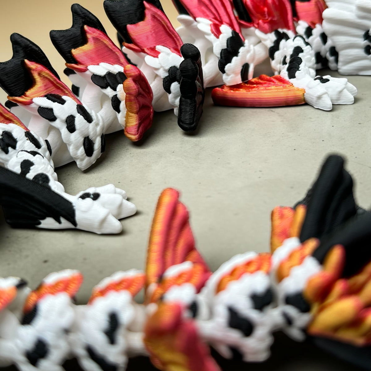 A close-up of a 3D-printed articulated dragon figurine with black, white, and red-orange scales, arranged on a neutral gray surface.