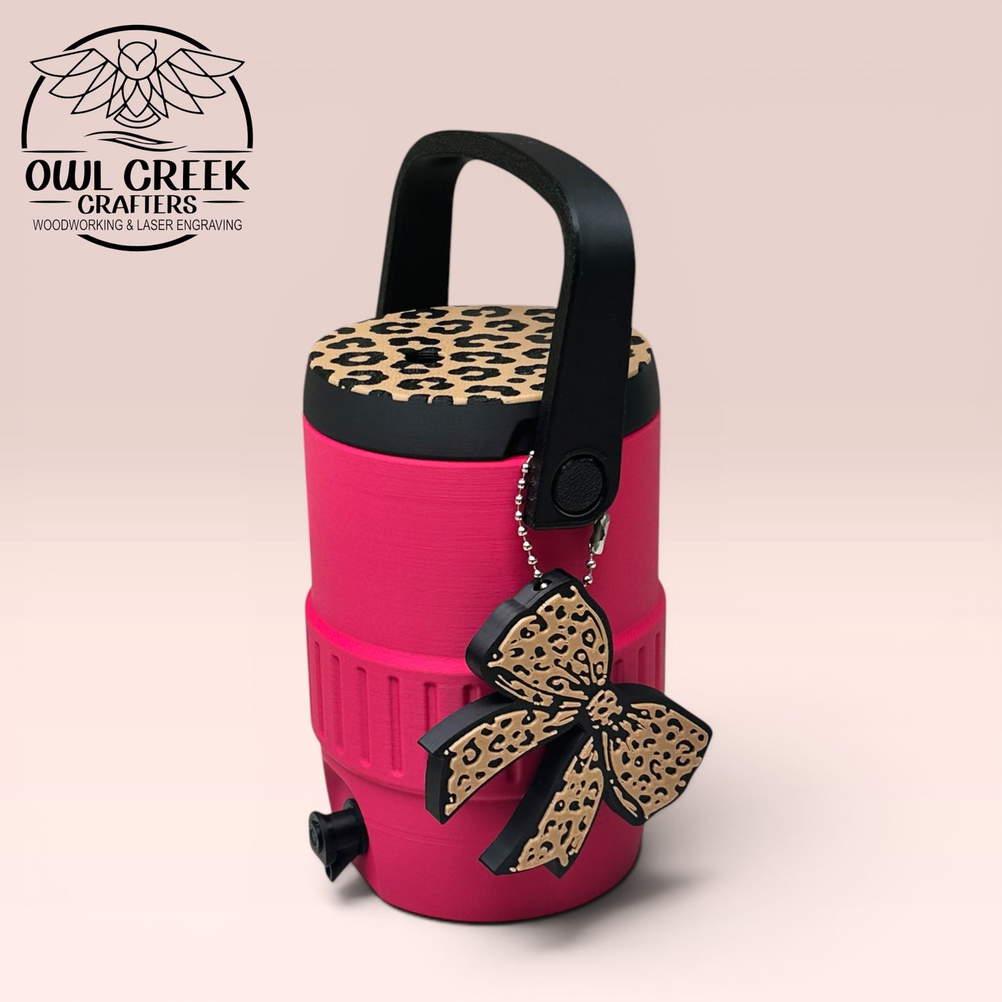 Pink can cooler coozie with leopard print lid, a black handle, and a leopard bow keychain, on a beige background with the Owl Creek Crafters logo.