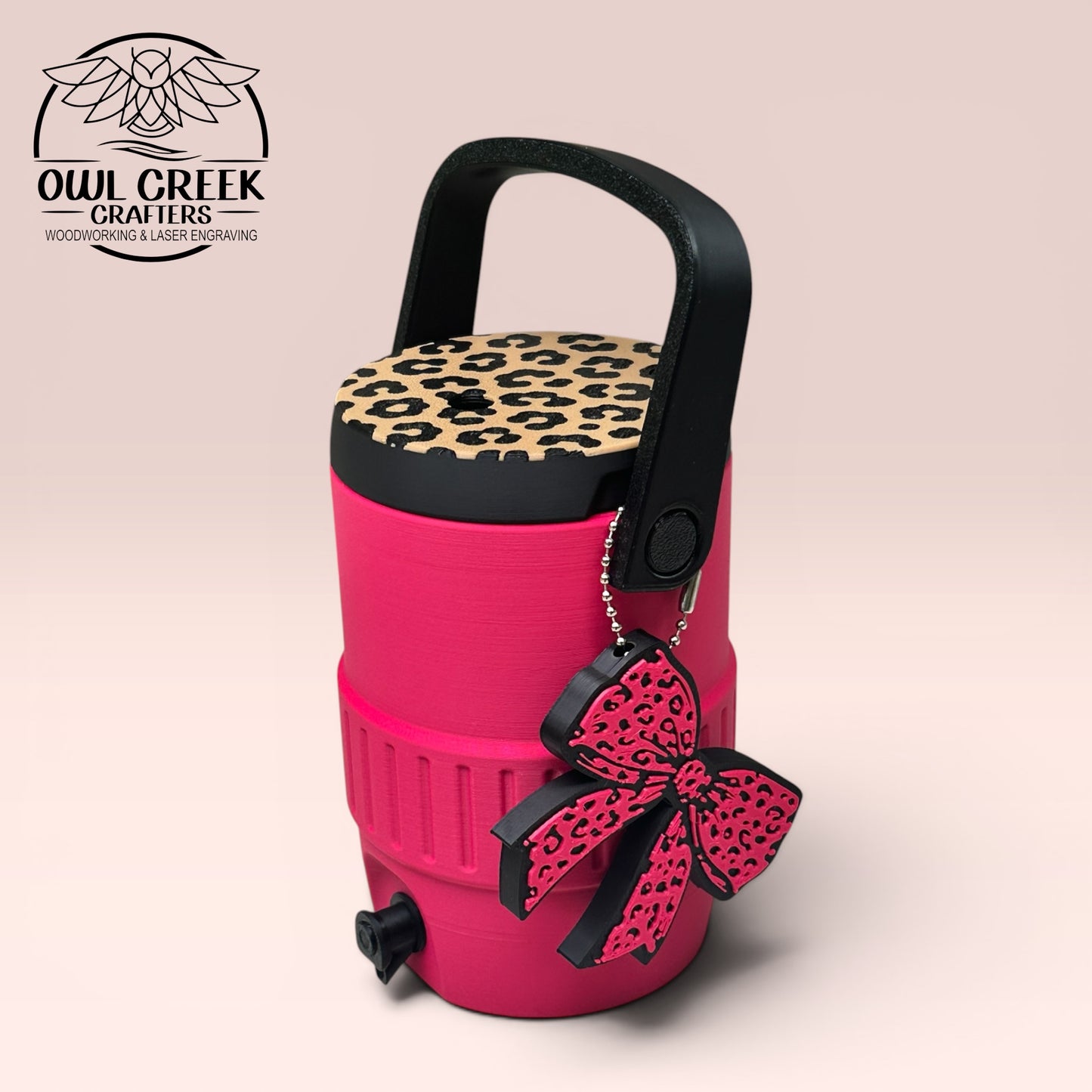 Pink can cooler coozie with leopard print lid, a black handle, and a pink leopard bow keychain, on a beige background with the Owl Creek Crafters logo.