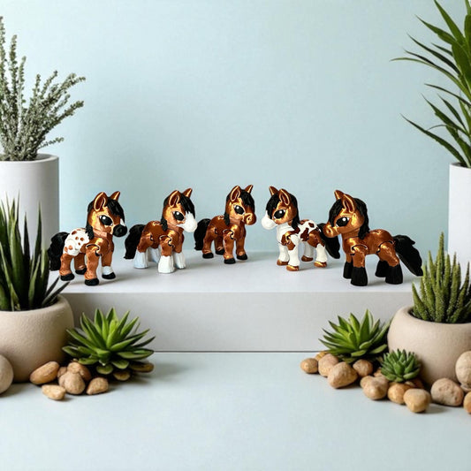 Set of five 3d printed toy horse figurines on a white surface with plants in the background