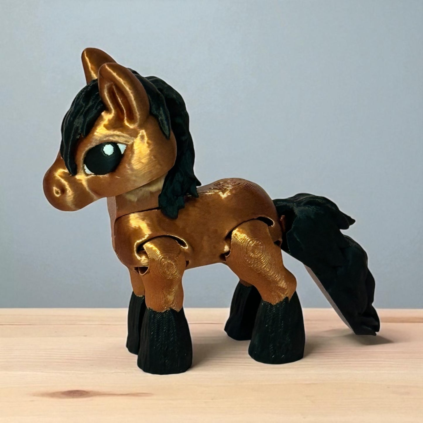 3d printed toy horse with golden brown and black coloring on a wooden surface with a grey background