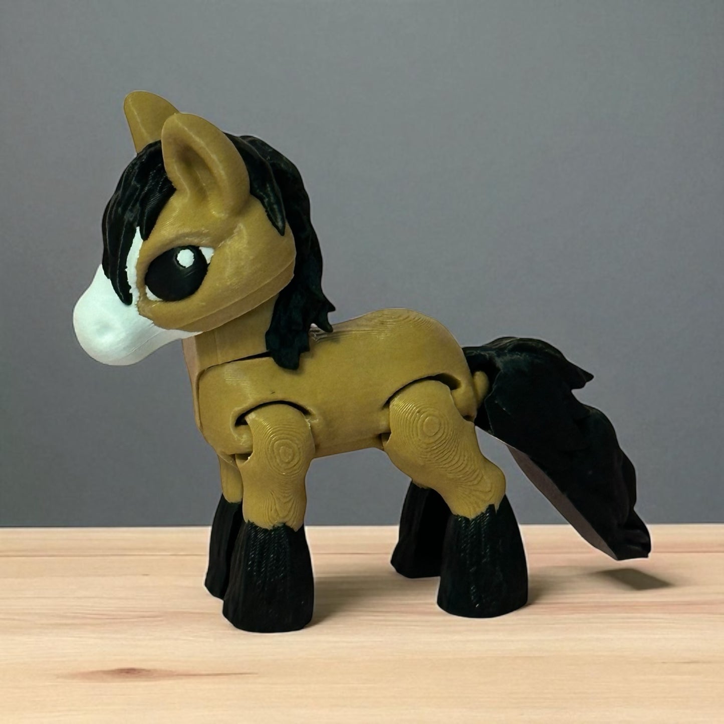3d printed brown toy horse figure with a white nose on a wooden surface with a gray background