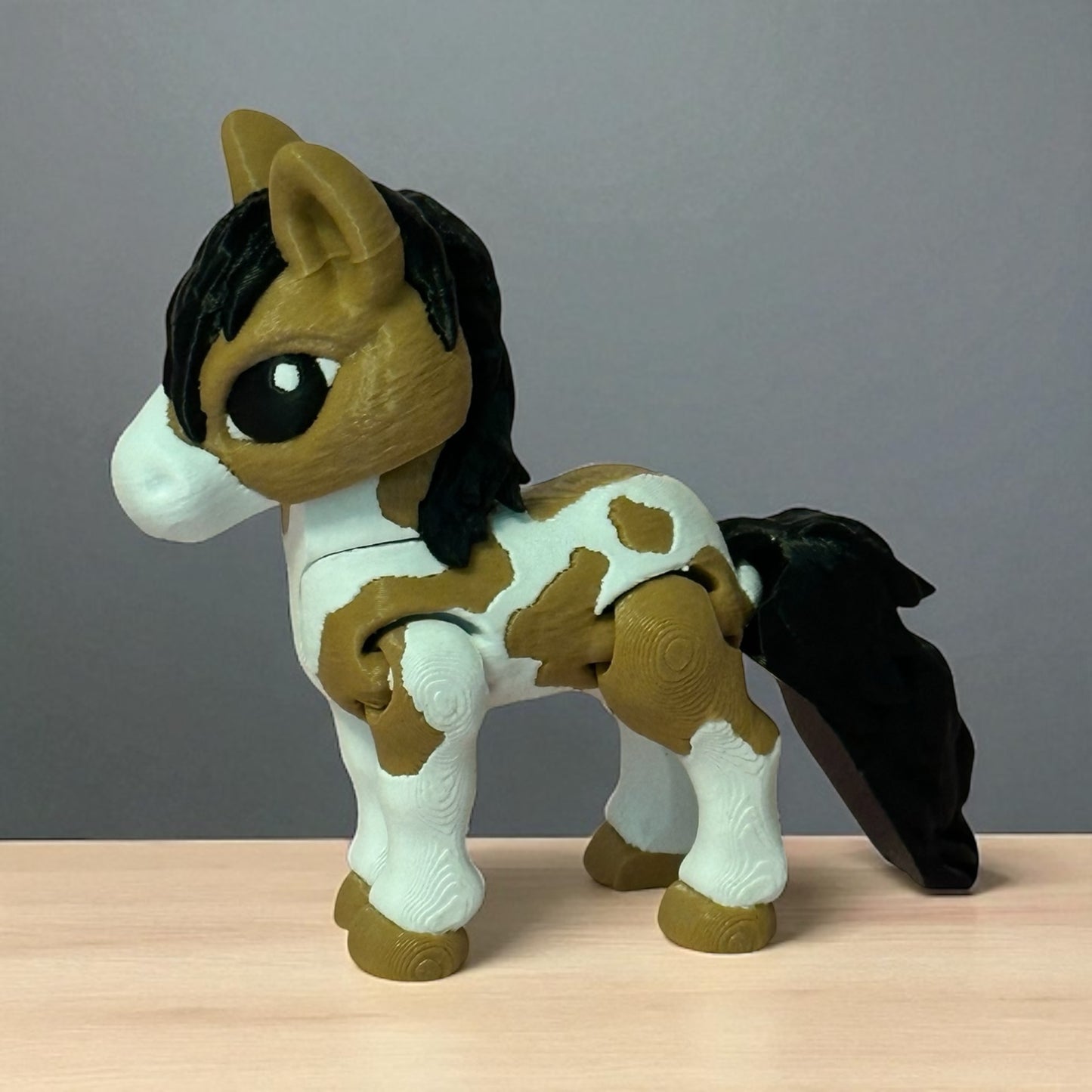 3d printed toy horse with brown and white pattern on a wooden surface and gray background