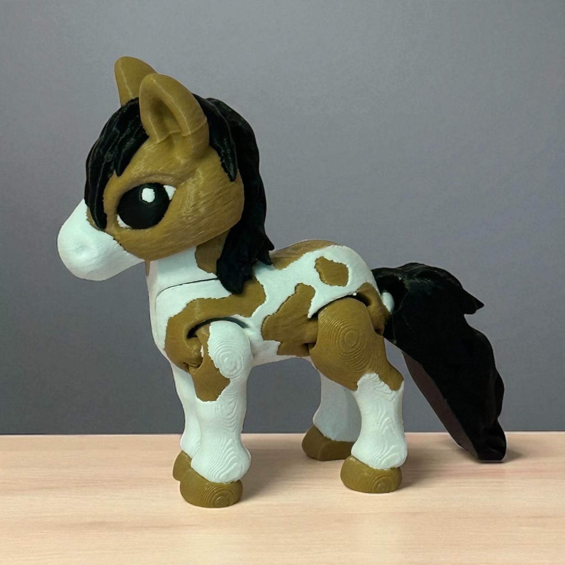 3d printed toy horse with brown and white pattern on a wooden surface and gray background