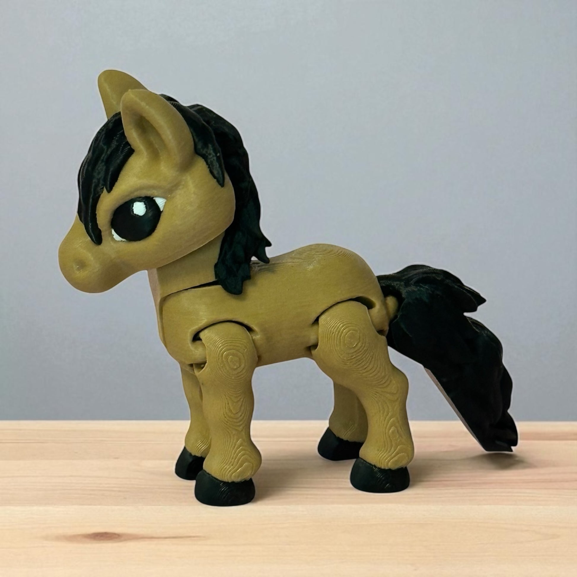 3D printed toy horse with black mane and tail on a wooden surface and grey background