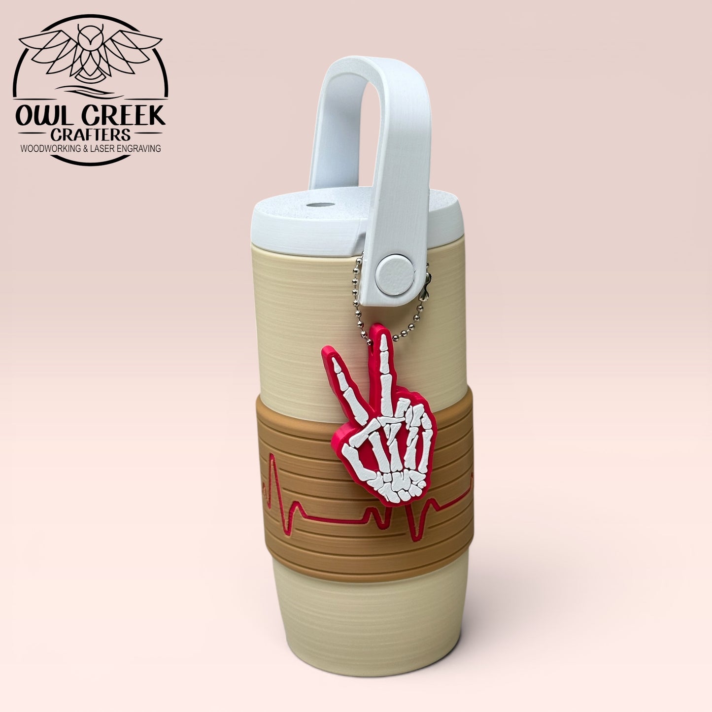 Beige and brown can cooler coozie with a magenta EKG design, with a magenta and white skeleton hand peace sign design keychain, and white handle and lid on a beige background, featuring Owl Creek Crafters logo