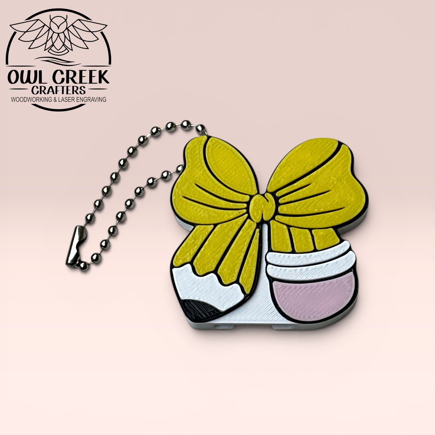 Bow in the shape and color of a pencil design keychain with a beige background and the Owl Creek Crafters Logo