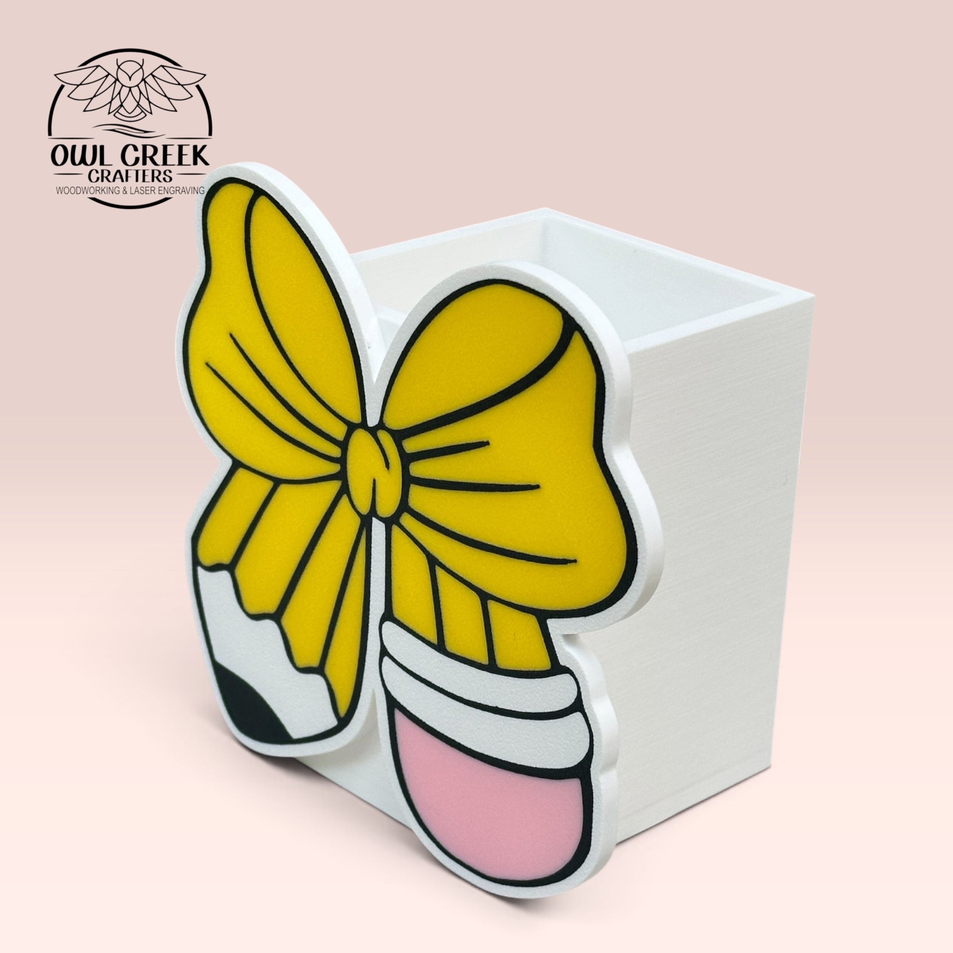 A 3d printed white pencil holder with a design in the front of a pencil in the shape of a bow. On a pink background with the Owl Creek Crafters logo in the top left corner
