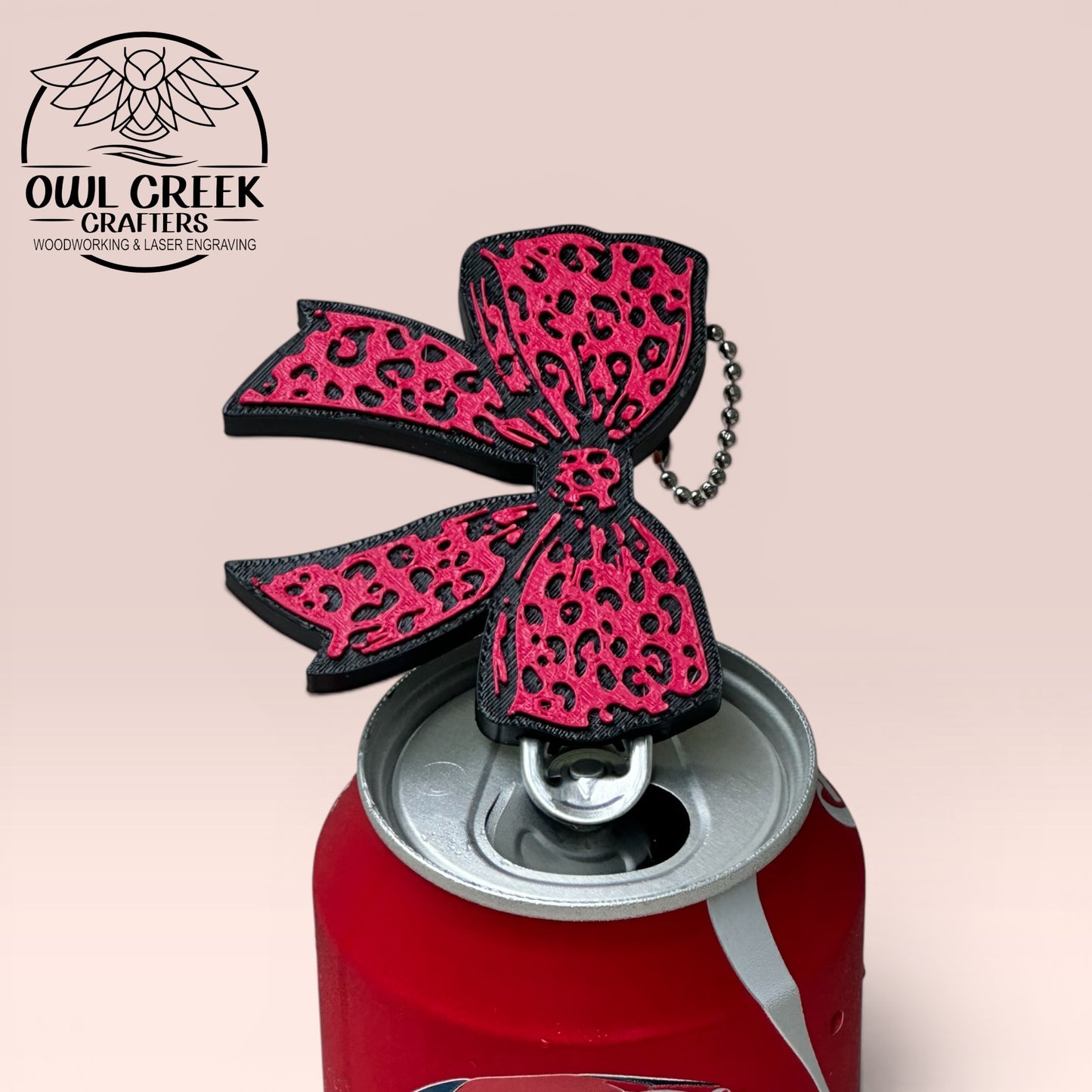 Pink leopard print bow keychain on a Coca-Cola can, with a beige background with 'Owl Creek Crafters' logo
