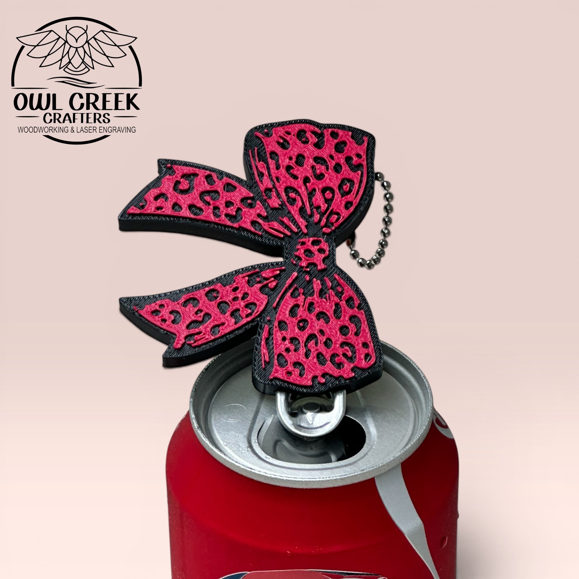 Pink leopard print bow keychain on a Coca-Cola can, with a beige background and the Owl Creek Crafters Logo