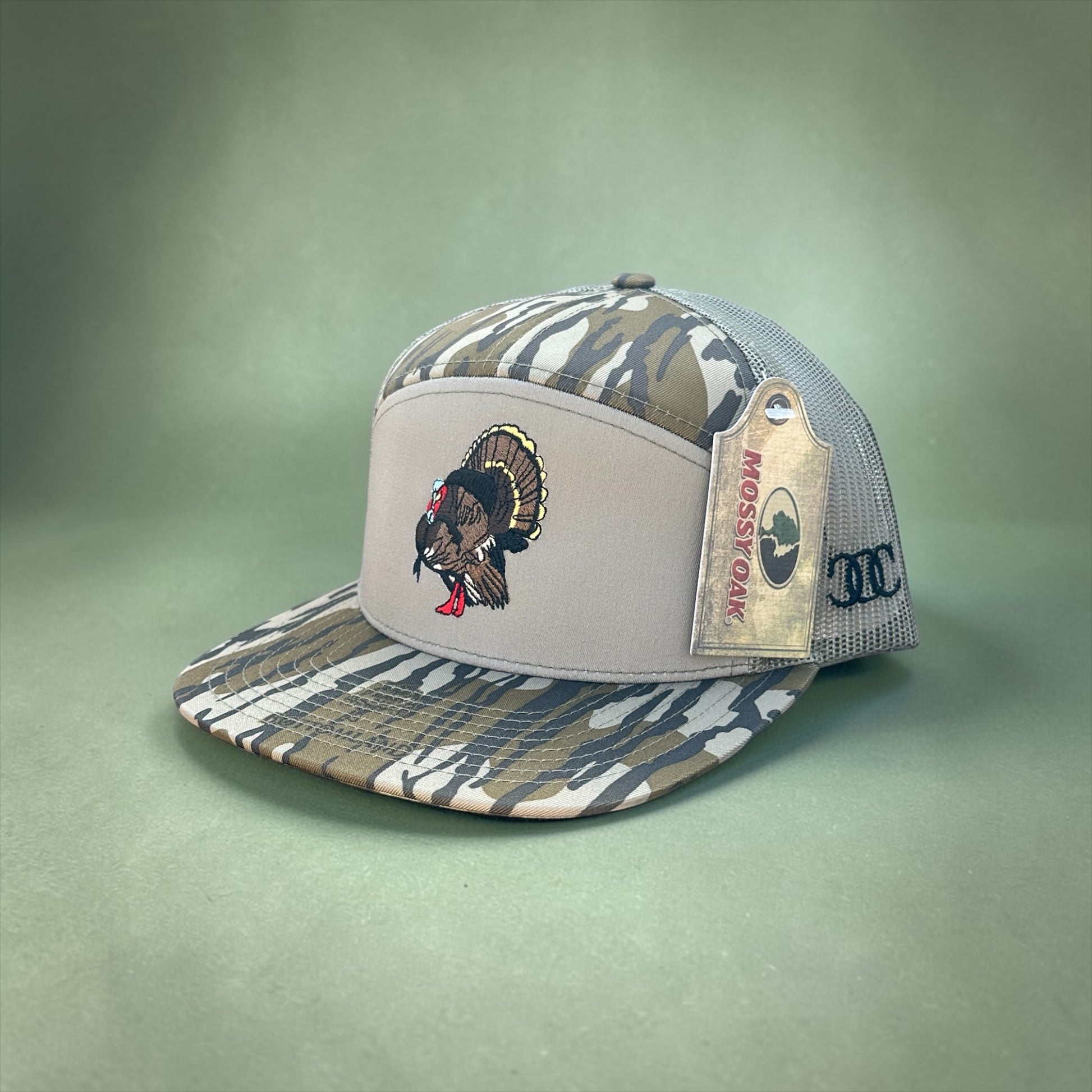 Camouflage and green trucker cap with an embroidered turkey design and mesh back with a brand logo tag on a green background