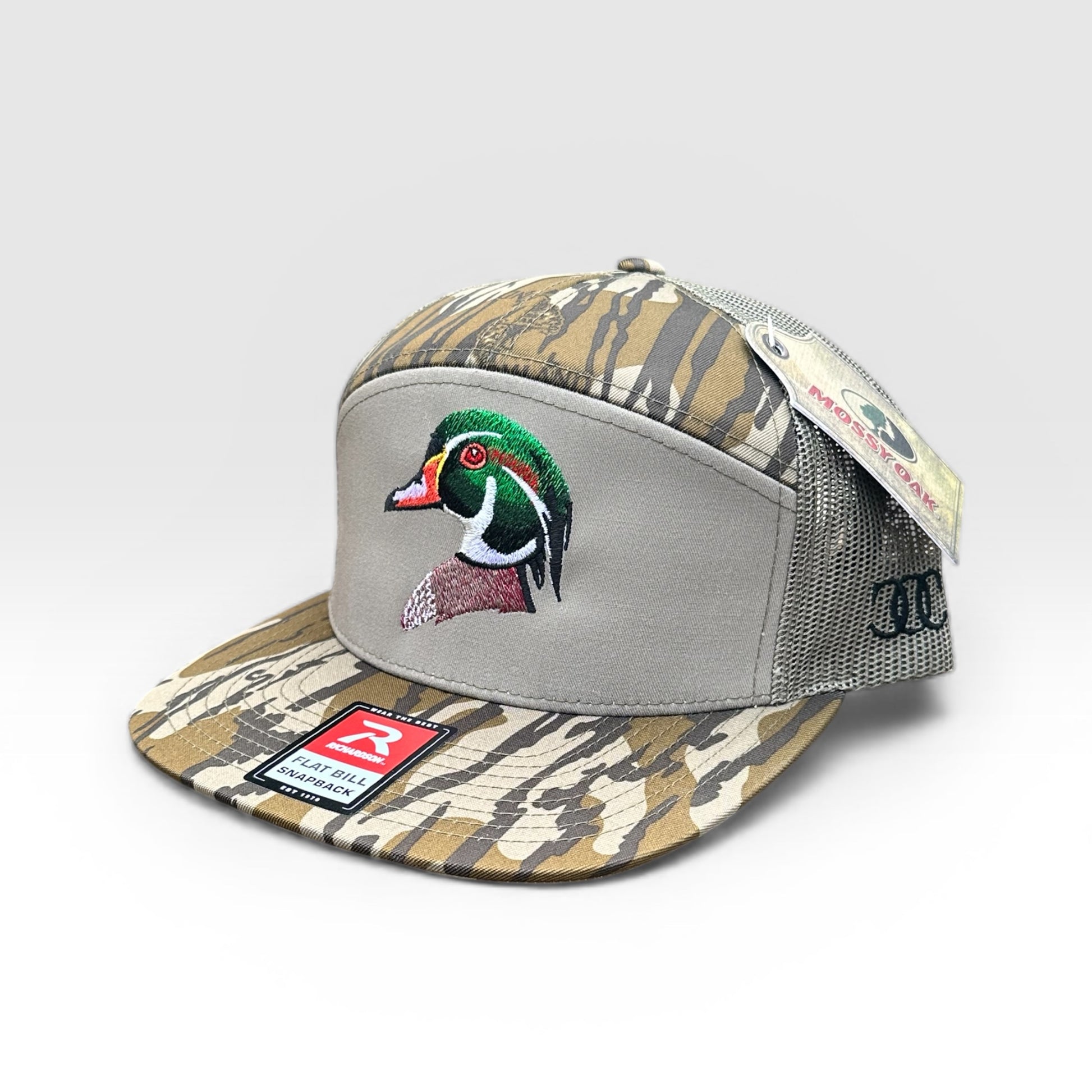 Bottomland camouflage and gray green trucker cap with an embroidered wood duck design on a white background