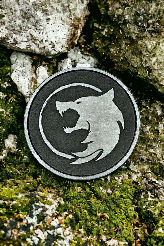 A silver coin with a white wolf design on a rock and moss background