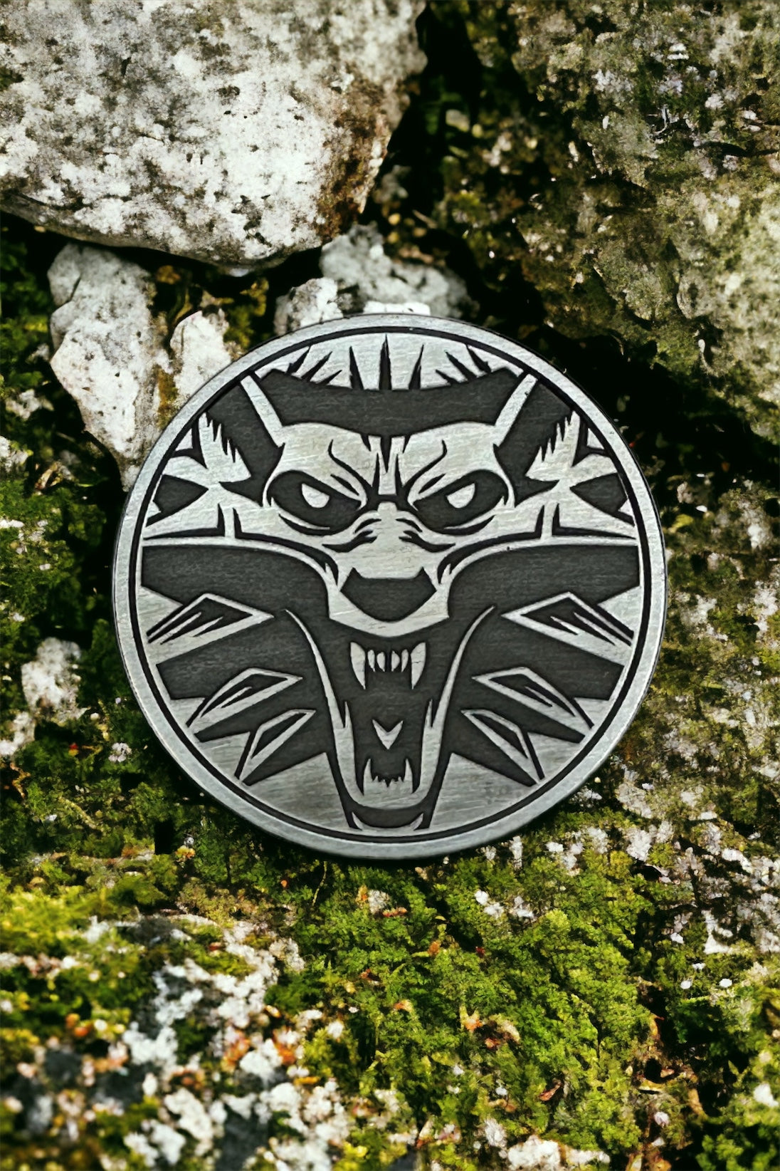 A silver coin with a white wolf design on a rock and moss background