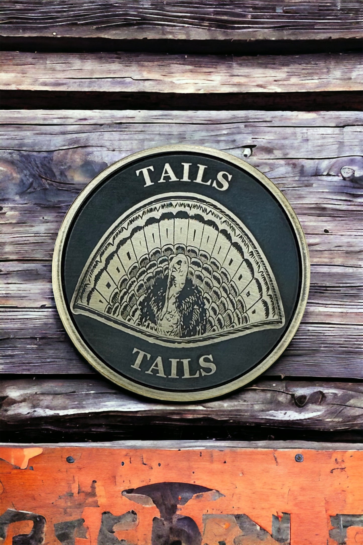 A double-sided solid brass coin with a laser engraved design of a turkey on it, with the text 'TAILS' around the edge. The coin is placed on a wooden surface.
