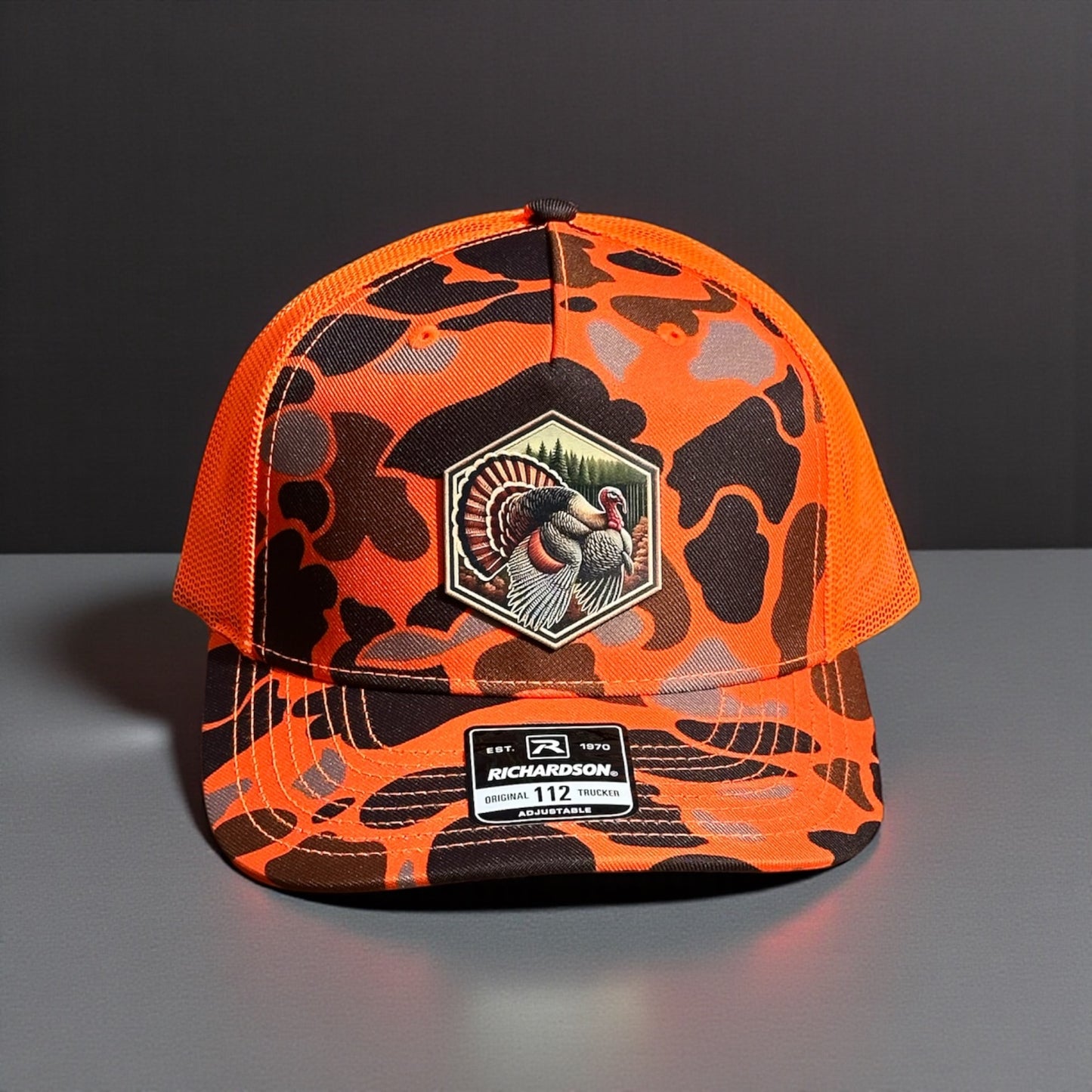 Orange and black camouflage trucker  cap with a hexagon turkey design patch on a gray surface and dark background